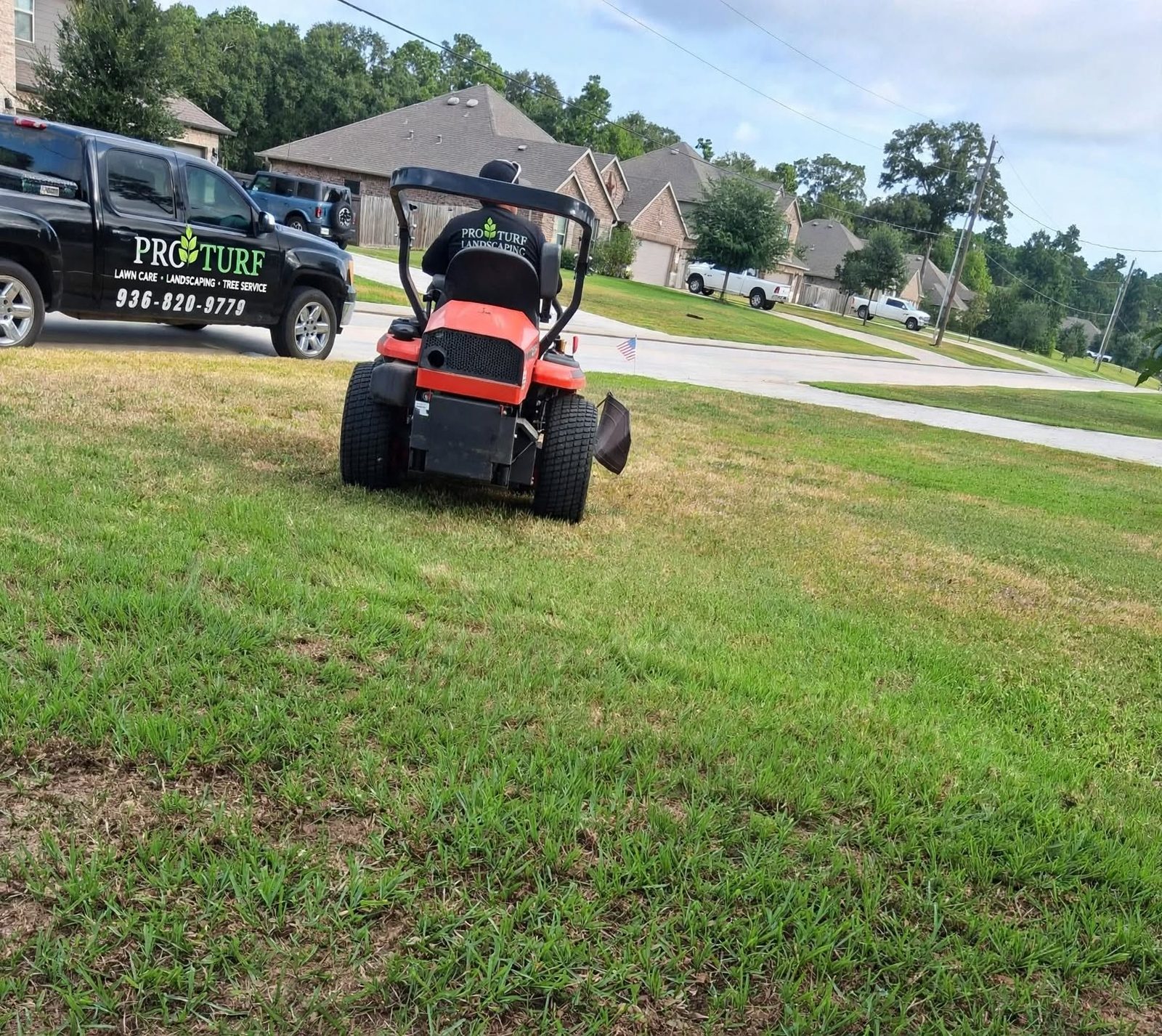 A Pro Turf Landscaping crew member mowing a lawn, company truck parked in the background