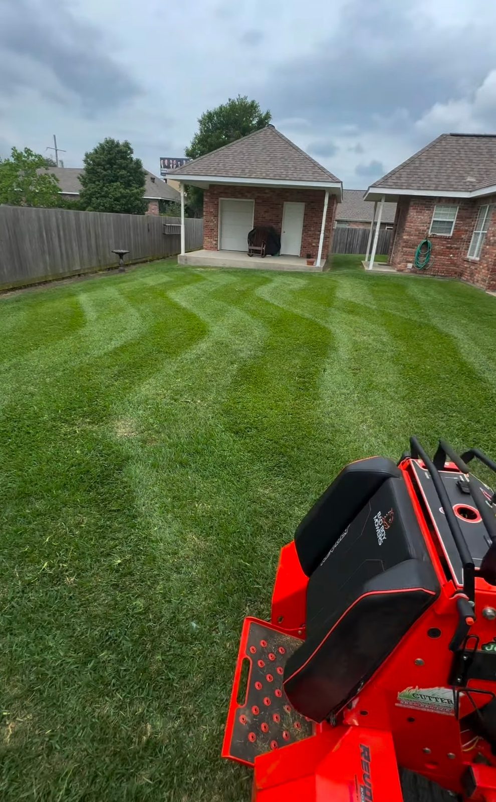 Freshly mowed backyard lawn with crisp mower stripes, zero-turn mower in foreground