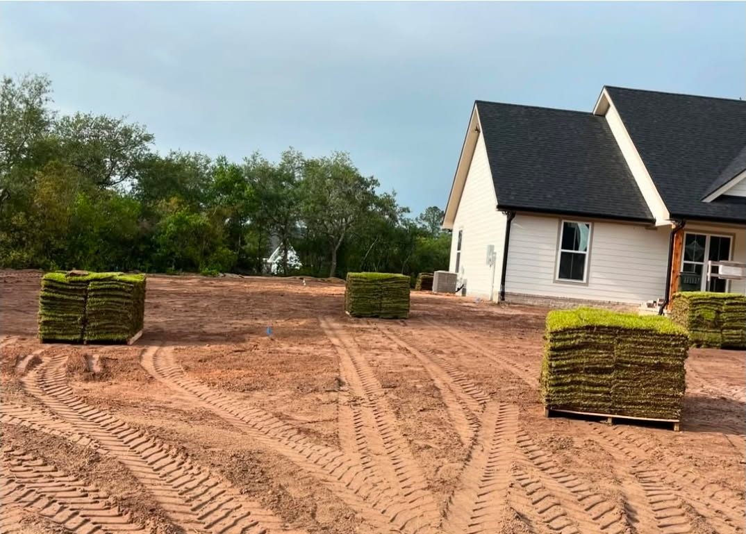 Pallets of sod staged on a graded dirt lot at a new-construction house, mid-job
